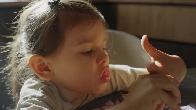 girl examines finger, young caucasian girl carefully studies her finger at table with pensive look