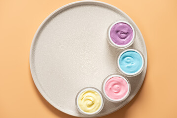 Set of cosmetic color creams in jars on round ceramic tray, top view, flat lay, copy space, skin care products