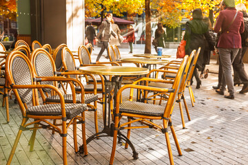 Outdoor cafe terrace with empty chairs and tables in autumn sunlight on a city street