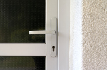 Sleek white door handle mounted on a textured metal-and-glass surface, featuring a secure lock mechanism. The surrounding stucco wall and frame add contrast to this modern architectural detail.