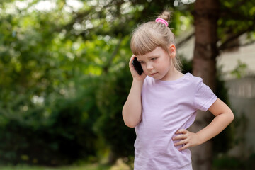 Young girl child talking on a smartphone outside, a kid during a phone call with a serious business...