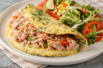 Omelette stuffed with canned tuna and peppers and served with vegetable salad close-up in a plate on the table. Horizontal