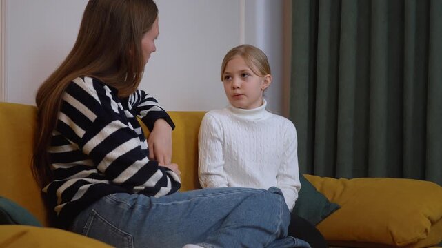 A psychologist mom and daughter are sitting on a comfortable yellow couch, engaging in a serious discussion, perhaps on a sensitive topic or a recent event