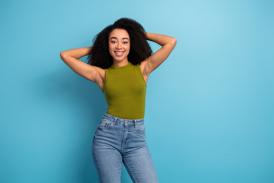 Charming young woman with natural curls posing confidently against a vibrant blue background wearing a casual chic outfit