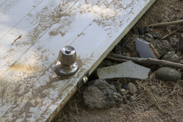 Broken white door with metal doorknob lies abandoned in scene of destruction. Dirty wood and debris...