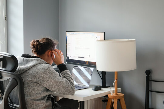 Man working at desk with two screens and headphones, his thinking about the project, back view. Focused freelancer editing digital content in modern home office setup