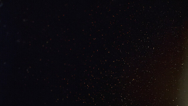 Dark abstract background with scattered dust particles, cinematic film grain texture, and subtle warm light. Perfect for retro photography effects, video overlays, and grungy design projects.