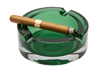 Isolated glass ashtray containing a lit cigar, resting in the depression on the rim edge