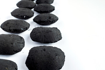 Row of black charcoal briquettes aligned diagonally on a bright white background with negative space: Perfect for barbecue, grilling, energy, and outdoor cooking advertisements or backgrounds