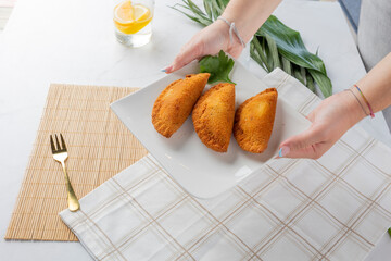Hands serving fried empanadas on white plate