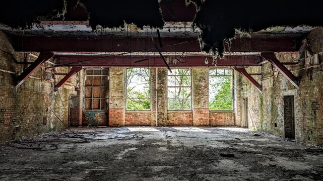 Derelict warehouse, dark abandoned industrial factory building interior. Darkness shadows, bright sunlight through broken windows. Collapsing ceiling insulation metal girders roof beams. Daylight ruin