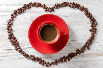 A red coffee cup with a saucer on a white wooden table, encircled by coffee beans with a heart shape formed from a chain of beans, isolated on a clean background