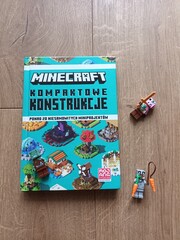 Naklejka premium Polish edition of the 'Minecraft Kompaktowe Konstrukcje' guide book for compact builds, featuring two Minecraft-themed toy figures on a wooden floor