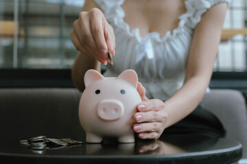A woman putting coins into a pink piggy bank, symbolizing saving money, financial planning, and...
