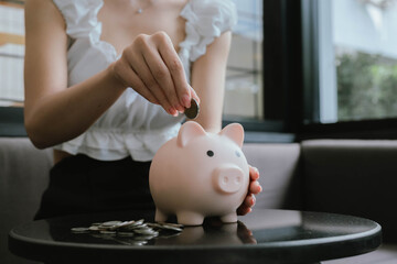 A woman putting coins into a pink piggy bank, symbolizing saving money, financial planning, and...