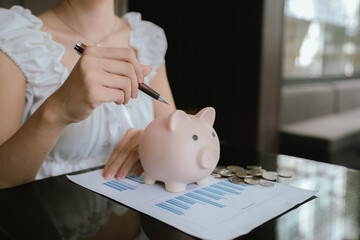 A woman putting coins into a pink piggy bank, symbolizing saving money, financial planning, and...