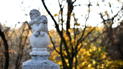 Fototapeta premium Ukraine, Kyiv 07.11.2024. angel statue in the park. little boy with wings. cupid statue in autumn park. figurine for design, marble sad angel sitting on a ball. blurred natural background. editorial