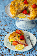 Piece of strawberry pie with lemon and fresh berries on lace light blue tablecloth