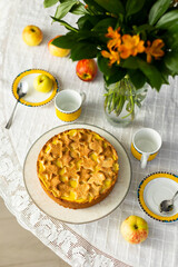 Homemade apple pie with custard cream on lace tablecloth, bouquet of red flowers and fresh apples