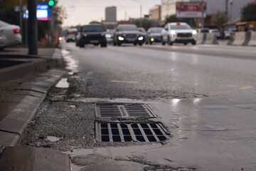 A drain on the road during rainy weather and moving cars in the background