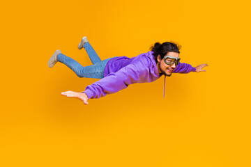 Young man in casual attire joyfuly posing while pretending to fly against a vibrant backdrop to convey energy and adventure.