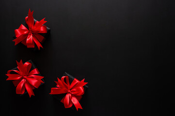 Black Friday background with three black gifts with vibrant red bows arranged in the corner against a dark background for copy space.