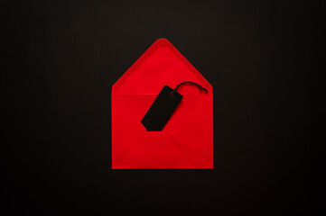 Black Friday concept with an open red envelope holds a black price tag on a dark background for signaling a secret sale.
