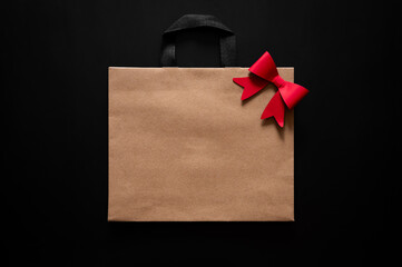 Black Friday concept with a brown paper bag with a red bow and black handles centered on a dark background.