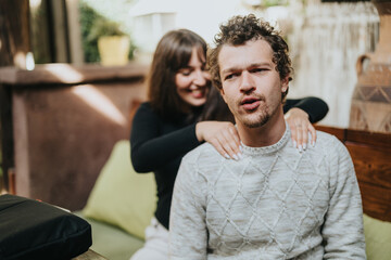 A woman joyfully provides a back massage to a man with a pensive expression, sitting outdoors in a...