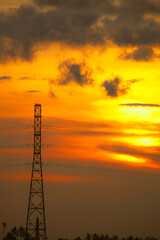 Naklejka premium The sunset silhouettes of the city's power line towers and communication antennas against a golden sky, reflecting industrial technology and construction.