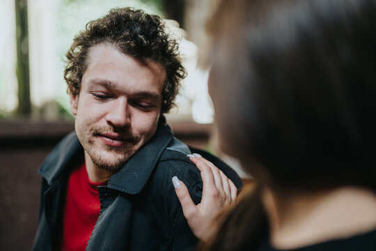 A man smiles warmly while a supportive hand rests on his shoulder, expressing care and encouragement. The close-up captures emotions of compassion, understanding, and connection in an outdoor setting.