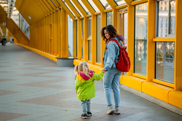 Fototapeta premium A little child girl and her young mother walk along a land crossing with a beautiful architectural yellow ceiling design in Moscow