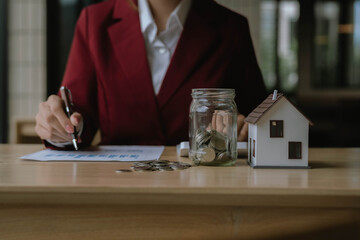 Businesswoman analyzing financial charts with a jar of coins and a small house model, representing investment, savings, and financial planning.