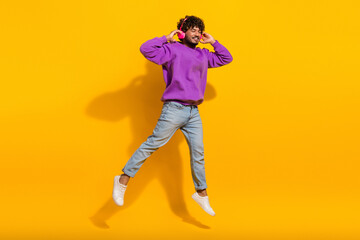 Young man in casual fashion with purple hoodie posing against vibrant yellow background expressing...