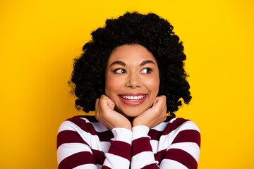 Cheerful young woman with curly hair looking up against yellow background in a striped top...