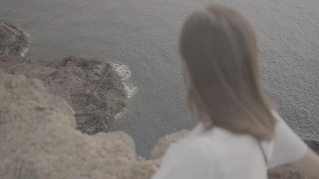 Over-the-shoulder shot of woman gazing down cliff to ocean in Madeira island Portugal (SLOG3)