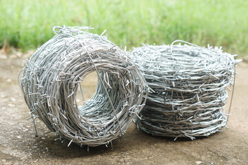 Close-up of two rolls of barbed wire placed on concrete ground with green grass background. Steel...