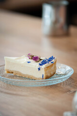 Close-up of a delicious cheesecake slice served on a glass plate, decorated with edible flowers — rosebuds and blue cornflower petals. Elegant dessert presentation on a wooden table, perfect for illus