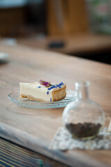 Close-up of a delicious cheesecake slice served on a glass plate, decorated with edible flowers — rosebuds and blue cornflower petals. Elegant dessert presentation on a wooden table, perfect for illus