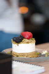 Close-up of a delicious cheesecake slice served on a glass plate, decorated with edible flowers — rosebuds and blue cornflower petals. Elegant dessert presentation on a wooden table, perfect for illus