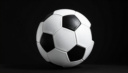 Fototapeta premium Classic black and white soccer ball with pentagon-hexagon pattern, isolated on solid black background