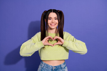 Smiling young woman making a heart gesture with her hands against a vibrant purple background