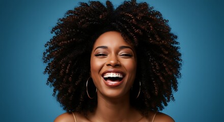 Joyful woman with curly hair smiles wide against blue backdrop