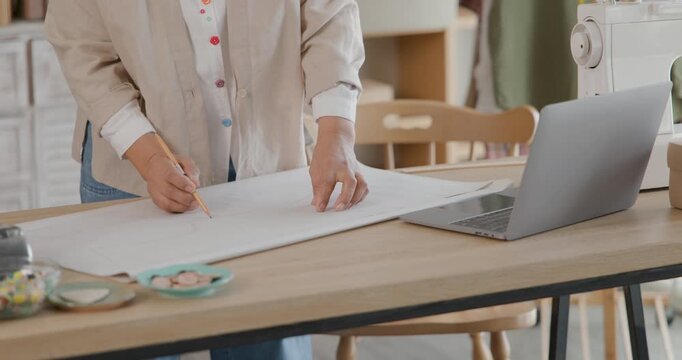female tailor carefully drafting clothing pattern by hand on craft paper using sewing template at work table in sewing studio, 4k video.