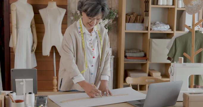female tailor carefully drafting clothing pattern by hand on craft paper using sewing template at work table in sewing studio, 4k video.