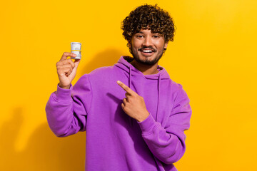 Fashionable young man in casual purple hoodie holding money and smiling against a yellow...