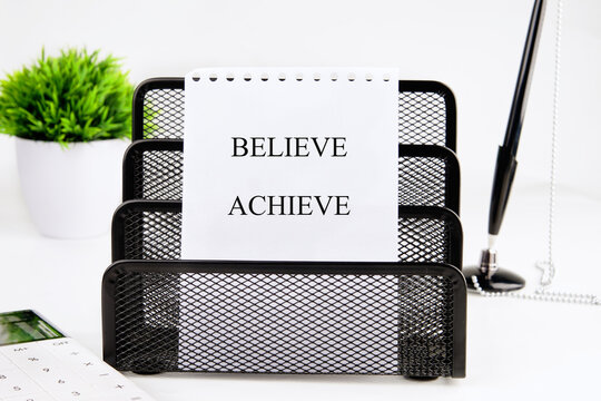 A clean workspace showcases a motivating note stating believe and achieve, alongside an organized desk with a plant, a calculator, and a penholder, promoting positivity and productivity
