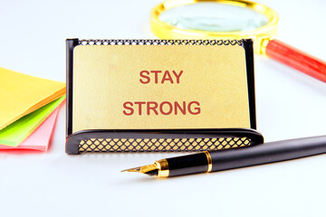 A bright workspace features a motivational note stating Stay Strong next to a shiny pen and colorful sticky notes, inspiring focus and resilience