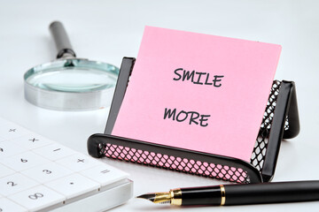 A vibrant pink note reads SMILE MORE, placed in a black desk organizer. Nearby, a calculator and pen await, creating a cheerful workspace atmosphere that invites positivity