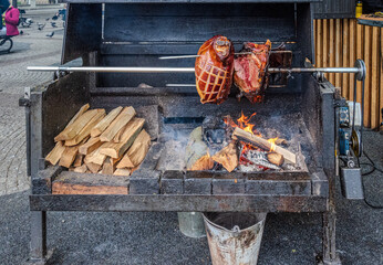 Traditional street-side wood-fired stove with large pieces of pork roasting on a metal rod, seen at a vendor’s stand in Prague Old Town, Czech Republic